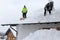 Two men shoveling high heavy snow from a house roof