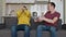 Two men sitting on the couch watch football match on TV and support different teams