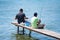 Two men sitting on small jetty fishing