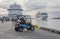 Two men sitting in a vehicle in the port and two huge ships in the background on cloudy weather