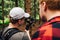 Two men stand on the nature in the woods and watch videos on the erkan filmed on camera with a stabilizer. Backstage photo two