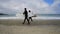 Two men in wetsuits carrying surfboards, walking along sandy shore of the Pacific Ocean