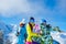 Two men and woman with snowboard and skis looking in different directions standing on snow resort against background of