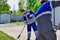 Two men in working overalls on a sunny summer day sweep the territory in the open air with brooms.