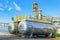 Two metal containers stand against the background of a gas processing plant