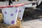 Two metal tin buckets painted with white paint with purple circles and a red rocker on them stand on a haystack