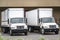 Two middle day cab semi trucks with box trailers standing on the warehouse dock loading cargo for the next local delivery