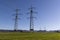 two mighty power poles on a green meadow in front of a cloudless blue sky in sunshine  in the daytime without people