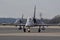 Two military jets positioned side-by-side on a tarmac runway under a cloudy sky