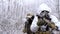 Two military men in white camouflage and green uniform, in winter forest. Soldiers with machinegun sneaking up alonge road, front