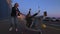 Two millennials girlfriends in street clothes have fun in a supermarket parking lot at sunset. Riding a shopping cart