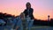 Two millennials girlfriends in street clothes have fun in a supermarket parking lot at sunset. Riding a shopping cart