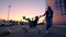 Two millennials girlfriends in street clothes have fun in a supermarket parking lot at sunset. Riding a shopping cart