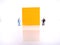 Two mini figure businessman Explaining Something at big blank orange standing sticky note