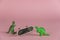 Two miniatures of dinosaurs and an upside-down mini skate against a pink background. Small green miniatures of predatory dinosaurs