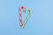 Two Mint hard candy canes striped in Christmas colours on blue background. Closeup. Heart sign