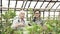 Two modern gardeners discussing plant care features working in a greenhouse. Agriculture, farming and gardening.