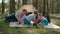 Two moms, two sons and Siberian Husky dog having fun on picnic blanket during summer family camping vacation with tent