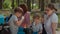 Two mothers and two sons drinking tea on picnic blanket during summer family camping vacation with tent in forest. Happy