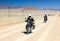 Two motorbikes driving fast on long straight desert road.