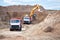 Two multi-ton mining trucks in process of loading ore by orange excavator for exporting minerals from the open-cast mine quarry