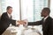 Two multiracial businessmen handshaking over office desk after e