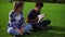 Two multiracial friends sitting on the green grass in park enjoying the day while holding cute little jack russell