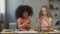 Two multiracial kids sitting at the table and smudging hands with paints