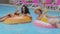 Two multiracial people Caucasian and Hispanic tanning women in swimsuit sunbathing sitting in tube floating inflatable