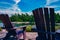 Two Muskoka chairs sitting on a wood dock facing a calm lake. Across the water is a white cottage nestled among green