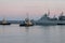 Two naval harbor tugs against the background of warships in the Petrovskaya pier of Kronstadt. Evening sunset. Russia