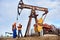 Two oil men standing by petroleum pump jack.