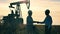 Two oil workers shaking hands with oil pumpjack operating in background