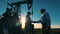 Two oil workers talking and shaking hands with pumpjack working in background