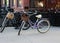 Two old-fashioned bikes with straw baskets on handlebars, set out for people to rent on sidewalk in front of shop, an easy way to