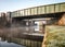 Two old green steel railway bridges crossing above canal river reflect in calm still water with boat passing underneath