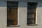 Two old windows with a broken stele boarded up with wooden plywood and metal on the brown concrete wall