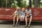 Two older brothers and little sister are relaxing in park on summer day. Portrait of siblings sit on bench