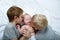 Two older brothers tenderly kiss and hug the younger child on a white bed. Happy family