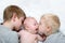 Two older brothers tenderly kiss and hug the younger child on a white bed. Happy family