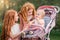 Two older redhead sisters are walking in the park on a sunny summer day with stroller with their younger sister. The girls try to