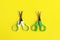 Two open baby green scissors on yellow background, flat lay with copy space. Baby care concept