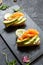 Two open sanwiches with dark bread, avocado, smoked salmon and radish, black background