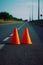 Two orange cones sitting on the side of road next to road. Generative AI