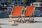 Two orange sun loungers stand on the shore of the blue water of a canal in Copenhagen. Denmark waiting for vacationers and tourist