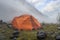 Two orange tents on the foggy morning in mountains