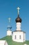 Two orthodox golden bright shiny crosses are on top of the black and blue cupolas of white old stone church with a green roof