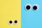 Two pair googly eyes on blue-yellow background look at each other. Mad funny toys eyes close up.