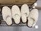 Two pairs of cozy fuzzy white home slippers on a metal shelf