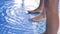 Two pairs of female legs stand on the side of the pool with blue clear water